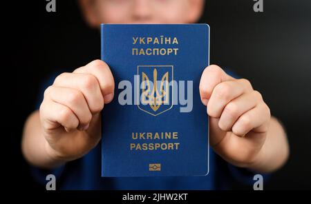 Ukrainischer internationaler biometrischer Pass in den Händen eines Kindes gesehen. Konzept für Reisen und Einwanderung. Stockfoto