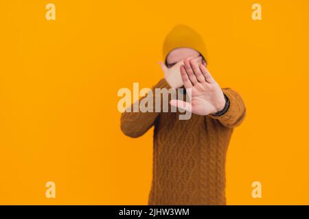Mann, der seine offene Handfläche zeigt und sein Gesicht bedeckt, schämt sich - Stop-Geste - orangefarbener Hintergrund. Hochwertige Fotos Stockfoto