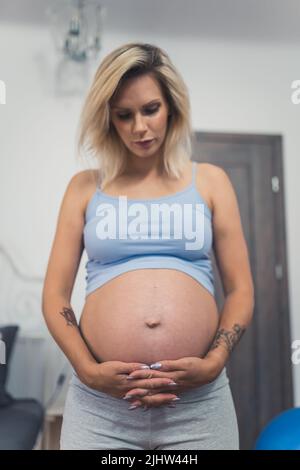 Vertikale mittlere Aufnahme einer blonden Schwangeren zu Hause. Hochwertige Fotos Stockfoto