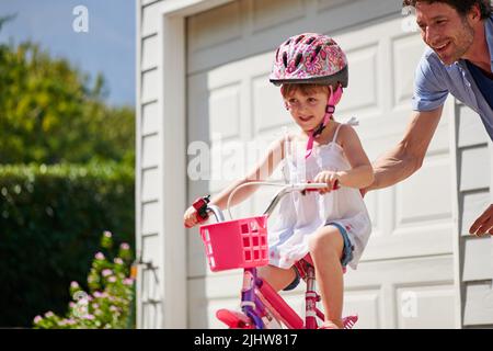 Ein junger Vater lehrt seine Tochter, Fahrrad zu fahren. Stockfoto