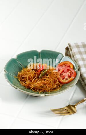 Bihun Goreng oder Stir Gebratene Vermicelli mit süßer Sojasauce Kecap und würzigen Chili. Serviert auf einer Keramikplatte über dem weißen Tisch Stockfoto