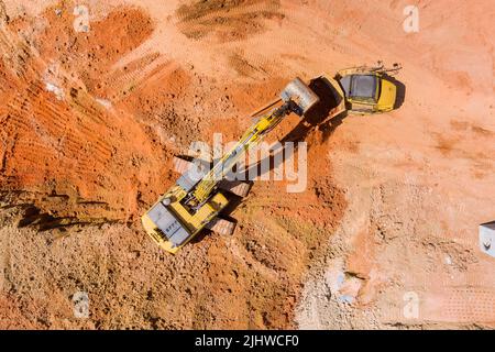 Auf einer Baustelle werden Aushubarbeiten durchgeführt, auf denen ein Bagger zum Verladen von Erde in einen Muldenkipper eingesetzt wird Stockfoto