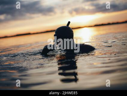 Junger Mann schnorchelt mitten im Meer bei Sonnenuntergang. Abenteuerlicher junger Mann mit Schnorchelausrüstung und Neoprenanzug. Stockfoto