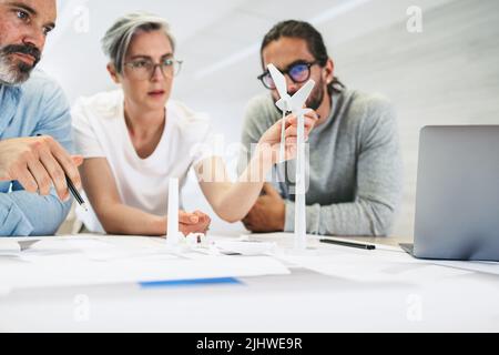 Innovative Geschäftsleute, die in einem modernen Büro mit 3D Windenergieanlagenmodellen arbeiten. Gruppe von kreativen Design-Profis, die während des Aufenthalts eine Diskussion führen Stockfoto