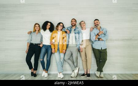 Multikulturelle Geschäftsleute, die die Kamera anlächeln, während sie zusammen gegen eine Wand stehen. Gruppe erfolgreicher Unternehmer, die als Tee zusammenarbeiten Stockfoto