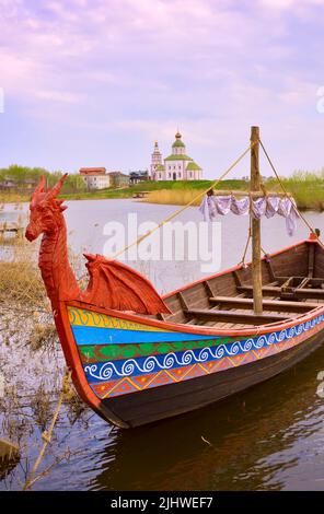 Touristenboot auf dem Wasser. Drakkar auf dem Fluss, Elijah Kirche am Horizont, Architektur des XVIII Jahrhunderts. Susdal, Russland, 2022 Stockfoto