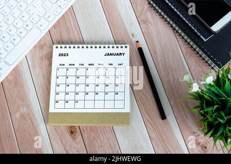 Weißer Januar 2023 Kalender gegen Holztisch. Direkt darüber. Flach liegend. Stockfoto