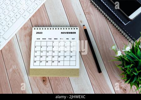 Weißer Tischkalender für November 2023 auf Holzschreibtisch. Direkt darüber. Flach liegend. Stockfoto