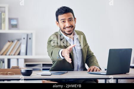 Es ist eine Freude, Sie zu treffen. Ein hübscher junger Geschäftsmann gestikuliert für einen Handschlag, während er in seinem Büro sitzt. Stockfoto
