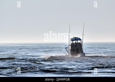 Ein privates Sportfischerboot fährt an einem sonnigen, nebligen Morgen durch den Indian River Inlet und hinaus in den Atlantischen Ozean. Stockfoto