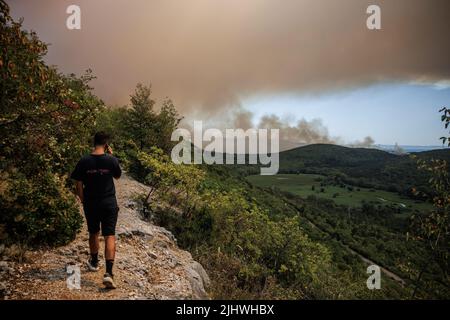 Doberdo Del Lago, Italien. 20.. Juli 2022. Ein Mann geht auf einem malerischen Pfad in einem Naturschutzgebiet in Doberdo del Lago, während ein großes Waldfeuer um das Dorf Jamiano in der Nähe von Triest wütet. Seit Sonntag, als ein großes Waldfeuer in der slowenischen Karstregion direkt über die Grenze ausbrach, sind in der Region Waldbrände ausgebrochen. (Foto: Luka Dakskobler/SOPA Images/Sipa USA) Quelle: SIPA USA/Alamy Live News Stockfoto