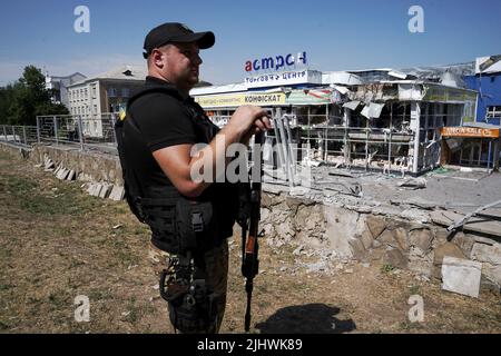 Nicht exklusiv: DRUZHKIVKA, UKRAINE - 9. JULI 2022 - Ein Polizeibeamter steht vor einem Einkaufszentrum, das durch den Beschuss russischer Truppen zerstört wurde, Dr. Stockfoto