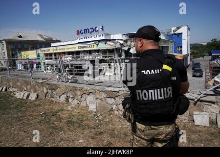 Nicht exklusiv: DRUZHKIVKA, UKRAINE - 9. JULI 2022 - Ein Polizeibeamter steht vor einem Einkaufszentrum, das durch den Beschuss russischer Truppen zerstört wurde, Dr. Stockfoto