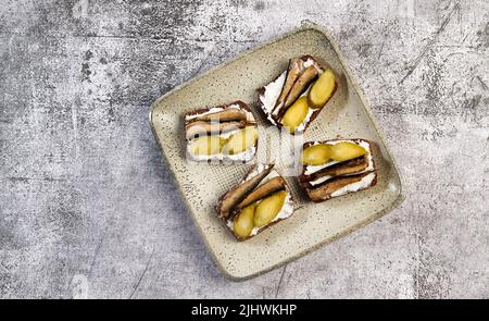 Sandwiches mit Sprossen, Quark und Gurken auf einem quadratischen Teller auf dunklem Grund. Draufsicht, flach liegend Stockfoto