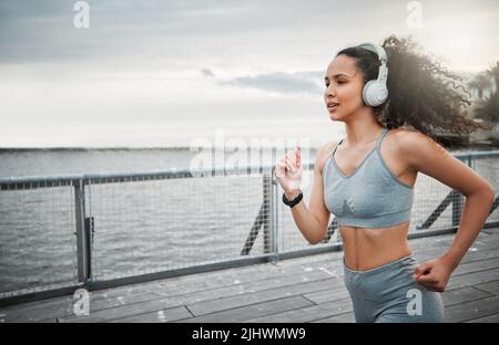 Auf zu den Rennen. Eine attraktive junge Sportlerin, die während ihres morgendlichen Laufs draußen Musik hört. Stockfoto