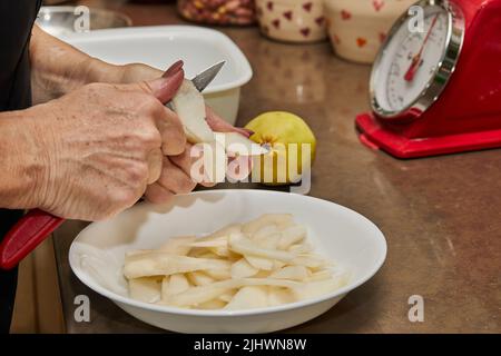 Der Koch schneidet die Birnen in Scheiben für den Schokoladenkuchen mit Birne und Nüssen. Schritt für Schritt Rezept. Stockfoto