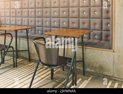 Café-Einrichtung mit gepolsterter und betonierter Wand, Metallstühlen und Holztischen. Selektiver Fokus. Stockfoto