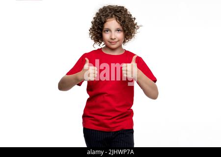 Positiv сurly kurzhaarige weibliche Kindermädchen 10-12 Jahre alt trägt rotes Basic T-Shirt. Lächelnd präteen schulmädchen zeigt zwei mag, Genehmigung Zeichen, Th Stockfoto