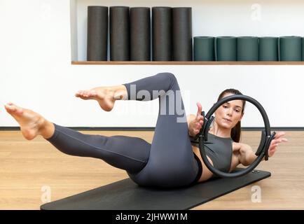 Focused Fit Damen in Sportbekleidung, die auf einer Matte liegt und die Beine streckt, während sie während des Fitnesstrainings mit Pilates Ring trainiert Stockfoto