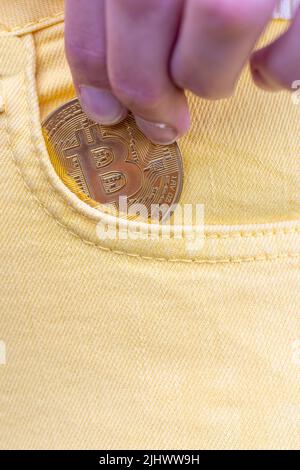 Nahaufnahme einer Frau, die Bitcoin in die gelbe Jeanstasche steckte, goldene Kryptowährung-Münze im Taschenhintergrund, Konzept der digitalen Währung virtuelles Geld. Hochwertige Fotos Stockfoto