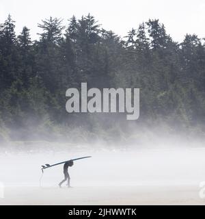 Junger Surfer mit Surfbrett im Nebel, Chesterman Beach, Tofino, Vancouver Island, British Columbia, Kanada. Stockfoto