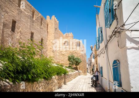 Eine Gasse, gesäumt von traditionellen blau-weißen Häusern, am Fuße der alten Mauern der befestigten Sousse Kasbah in der Medina von Sousse, Tunesien. Stockfoto