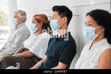 Wir müssen alles in unserer Möglichkeiten tun, um die Ausbreitung einzudämmen: Eine Gruppe von Menschen, die Gesichtsmasken tragen, während sie in einer Schlange sitzen. Stockfoto