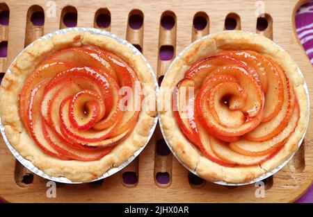 Frisch gebackene hausgemachte rosenförmige Apfeltörtchen auf Holzbrett Stockfoto