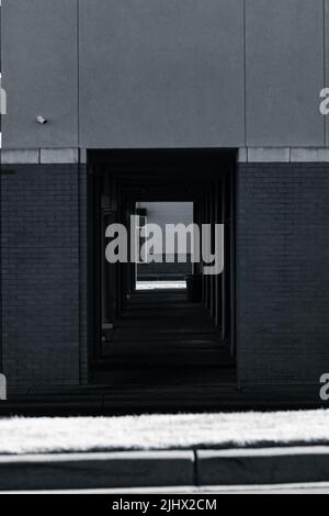 Eine vertikale Aufnahme eines dunklen Durchgangs unter einem modernen Gebäude von einer Seite der Straße auf die andere Seite Stockfoto