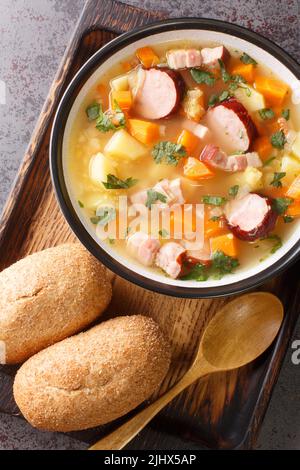 Hausgemachte herzhafte Erbsensuppe mit Gemüse, Speck und Würstchen in einer Schüssel auf dem Tisch. Vertikale Draufsicht von oben Stockfoto
