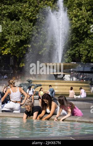 An einem der heißesten Tage in Großbritannien im Sommer, dem 2022. Juli, sitzen sich die Menschen mit ihren Beinen in den Springbrunnen am Trafalgar Square abkühlen. Stockfoto