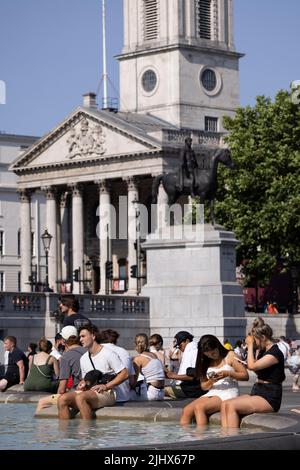 An einem der heißesten Tage in Großbritannien im Sommer, dem 2022. Juli, sitzen sich die Menschen mit ihren Beinen in den Springbrunnen am Trafalgar Square abkühlen. Stockfoto