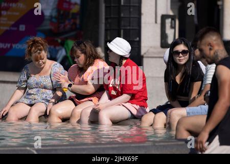 An einem der heißesten Tage in Großbritannien im Sommer, dem 2022. Juli, sitzen sich die Menschen mit ihren Beinen in den Springbrunnen am Trafalgar Square abkühlen. Stockfoto