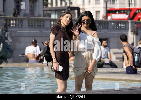 An einem der heißesten Tage in Großbritannien im Sommer, dem 2022. Juli, sitzen sich die Menschen mit ihren Beinen in den Springbrunnen am Trafalgar Square abkühlen. Stockfoto