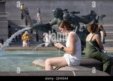 An einem der heißesten Tage in Großbritannien im Sommer, dem 2022. Juli, sitzen sich die Menschen mit ihren Beinen in den Springbrunnen am Trafalgar Square abkühlen. Stockfoto