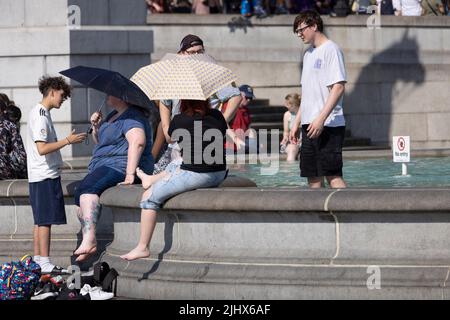 An einem der heißesten Tage in Großbritannien im Sommer, dem 2022. Juli, sitzen sich die Menschen mit ihren Beinen in den Springbrunnen am Trafalgar Square abkühlen. Stockfoto