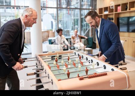 Zwei Geschäftsleute spielen Tischfußball am Tischfußball in der Lounge des Unternehmens Stockfoto