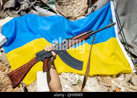 Das Gewehr wurde vor der ukrainischen Flagge auf Ruinen hochgehoben Stockfoto