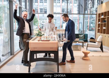 Der Geschäftsmann gewinnt Tischfußball am Tischfußball im Büro und jubelt Stockfoto