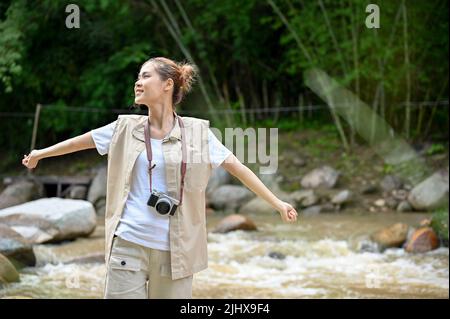 Schöne junge asiatische weibliche Reisende in der Nähe des Flusses und immer etwas frische Luft, um ihren Tag zu erfrischen. Camping- oder Trekkingkonzept Stockfoto