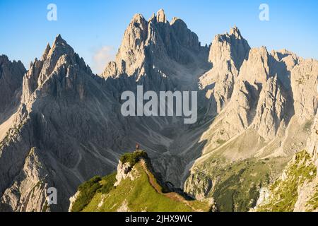 Atemberaubende Aussicht auf einen Touristen auf der Spitze eines Hügels, der den Blick auf die Cadini di Misurina während des Sonnenaufgangs genießt. Stockfoto