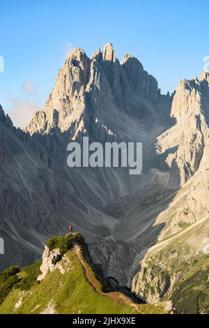 Atemberaubende Aussicht auf einen Touristen auf der Spitze eines Hügels, der den Blick auf die Cadini di Misurina während des Sonnenaufgangs genießt. Stockfoto