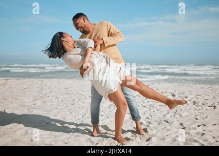 Liebevolles junges gemischtes Paar, das am Strand tanzt. Glücklicher junger Mann und verliebte Frau genießen romantische Momente während der Flitterwochen am Meer Stockfoto