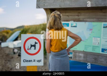 Ausgewählter Fokus der Bekanntmachung Zeichen für Hundebesitzer zu reinigen Hund poo Exkrement nach Fouling Frau im Hintergrund Stockfoto