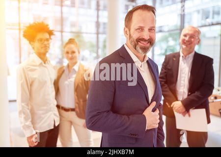 Erfolgreicher Geschäftsmann, der lächelnd vor seinem Geschäftsteam im Büro steht Stockfoto
