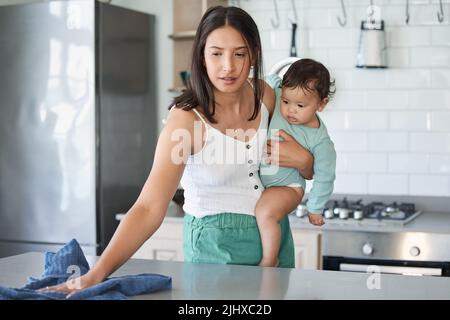 Eine Mutter hat immer eine Hand. Eine Frau putzt ihr Haus mit ihrem Baby auf ihrem Arm. Stockfoto