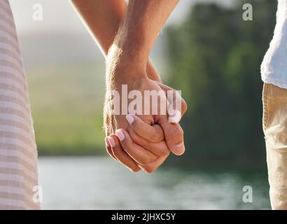 Ein unverkennbares Paar hält sich die Hände, während es Zeit an einem See verbringt. Stockfoto