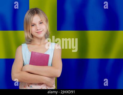 Junge glückliche Kind Mädchen mit blonden Haaren halten Buch vor schwedischer Flagge Hintergrund. Schule und Bildung in Schweden Konzept Stockfoto