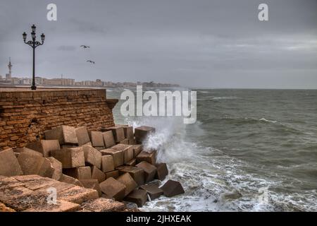 Wellen brechen gegen die Steinmauern der Promenade von Cadez, Spanien Stockfoto