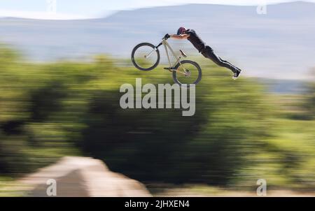 Junger Mann, der seine Radfahrkünste zeigt, während er draußen auf dem Fahrrad unterwegs ist. Adrenalin-Junkie übt einen Dirt-Jump im Freien. Mann trägt einen Helm Stockfoto